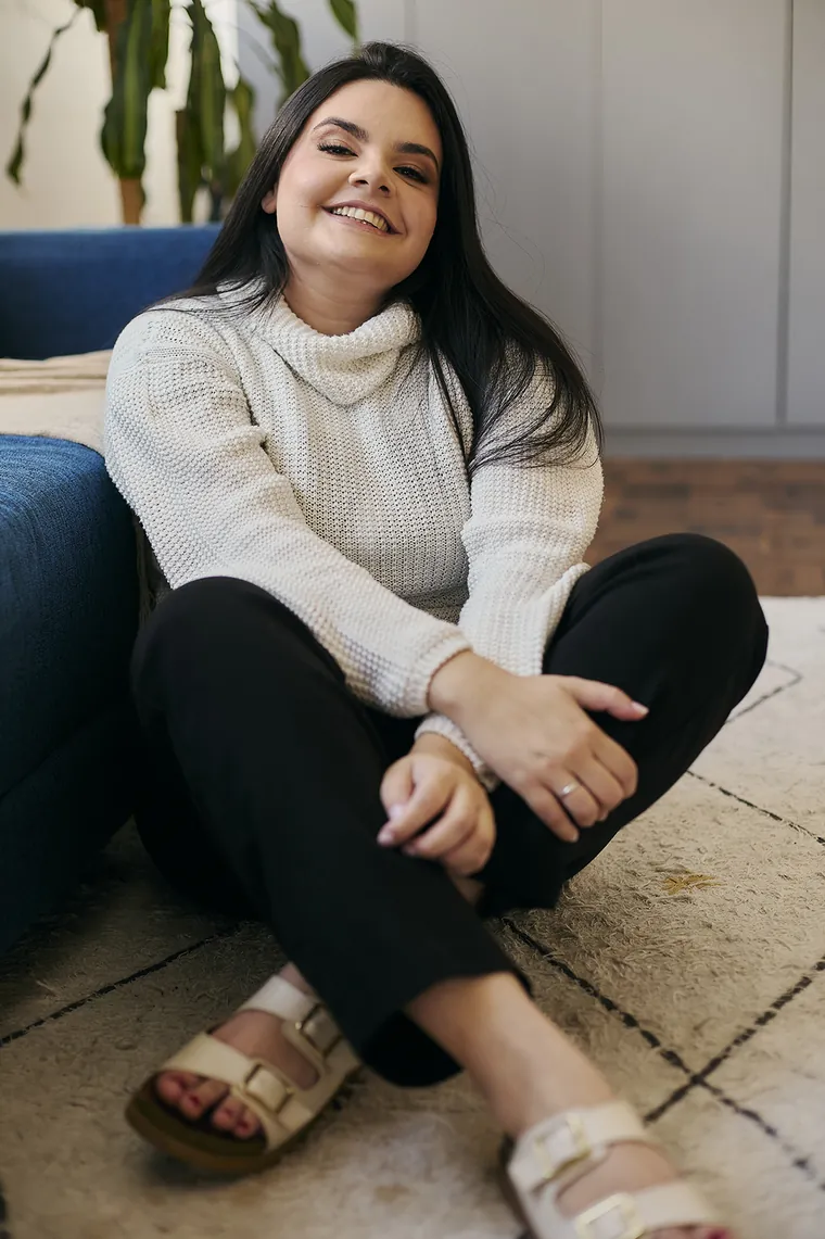 Jennifer da Luz Silva sorrindo, sentada em um tapete, em um ambiente acolhedor
