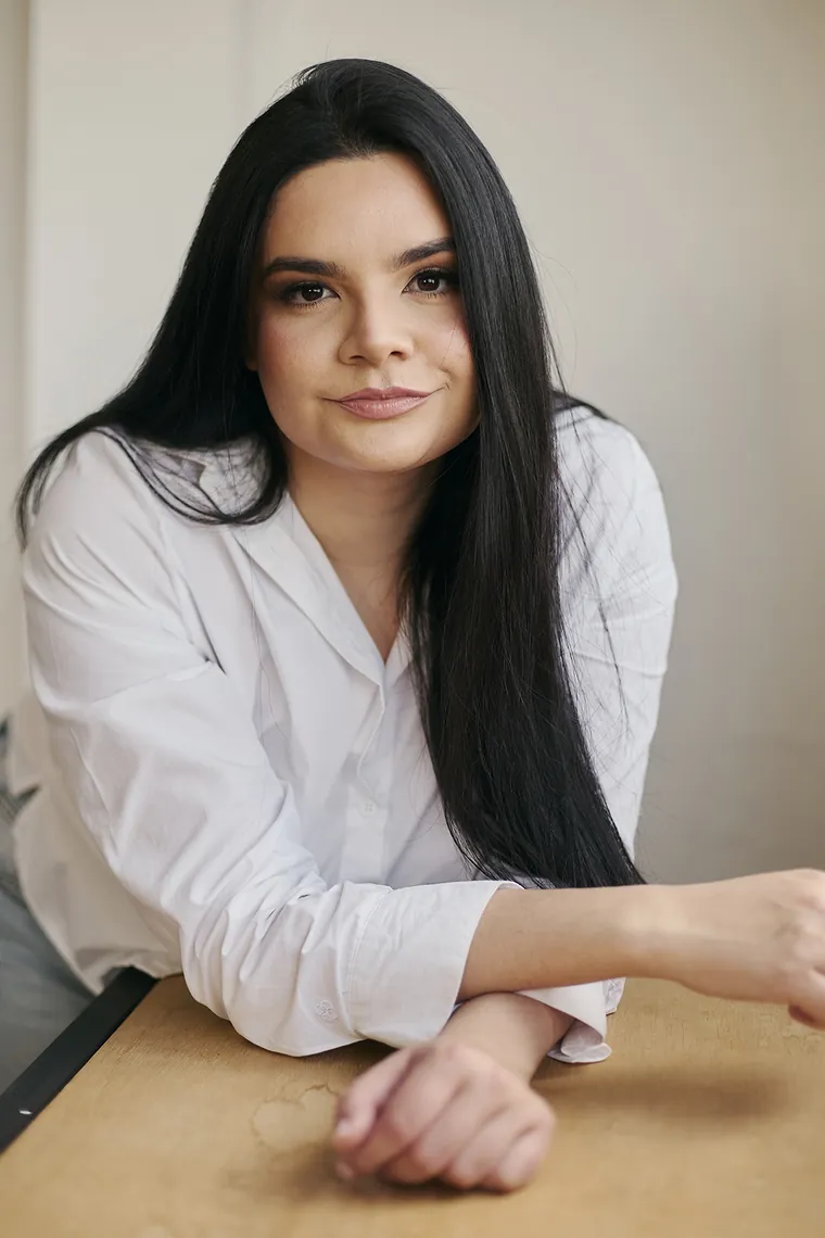 Jennifer da Luz Silva, psicóloga clínica, apoiada em uma mesa, olhando para a câmera