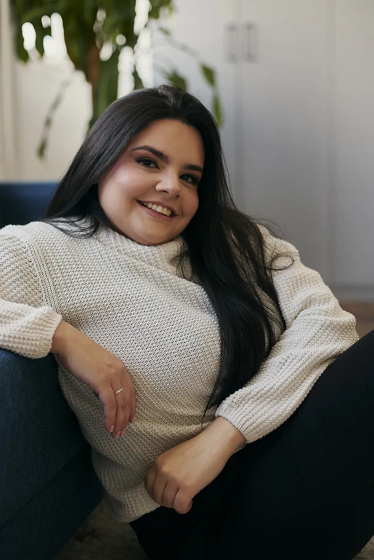 Jennifer da Luz Silva sorrindo, sentada no chão e recostada em um sofá azul
